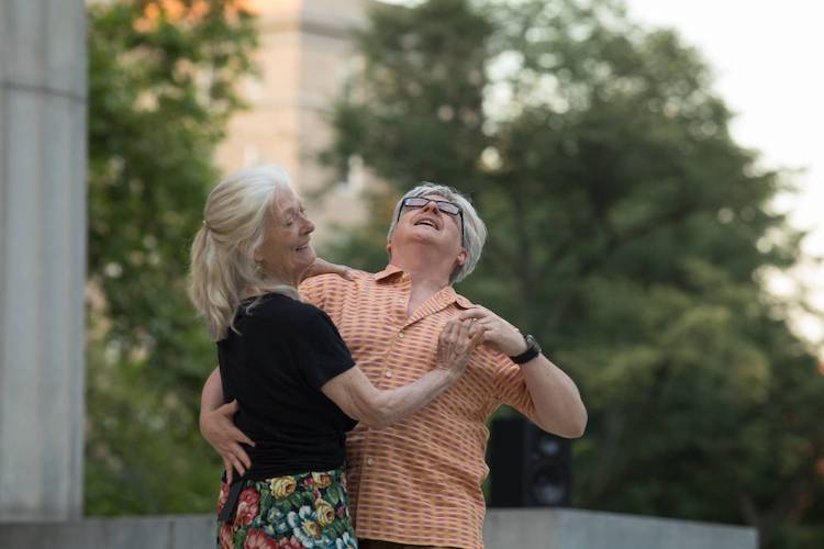 A white-haired woman faces a gray haired man as they dance close together.